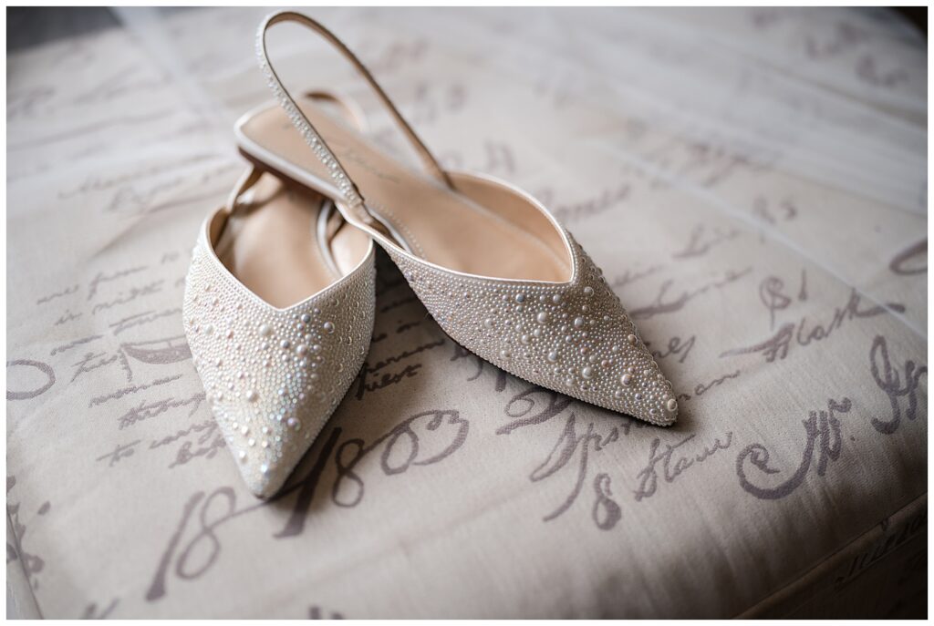 a detail photos of brides wedding shoes. They are cream color and covered in pearls.